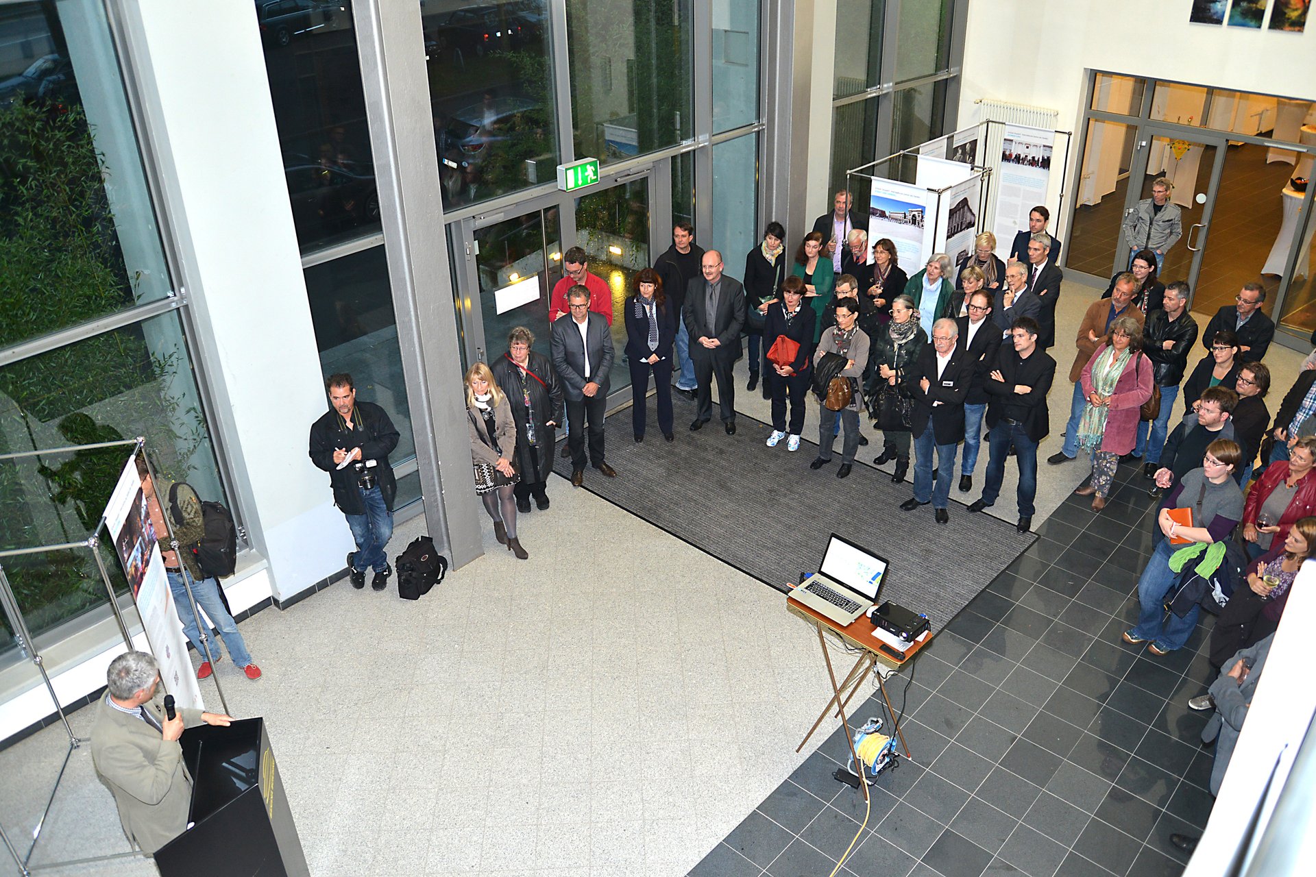 Mehrere Menschen stehen in einem großen Raum, links im Bild ein Mann an Stehpult der zum Publikum spricht. (Foto: Kammergruppe Pirmasens) Mehrere Menschen stehen in einem großen Raum, links im Bild ein Mann an Stehpult der zum Publikum spricht. (Foto: Kammergruppe Pirmasens)