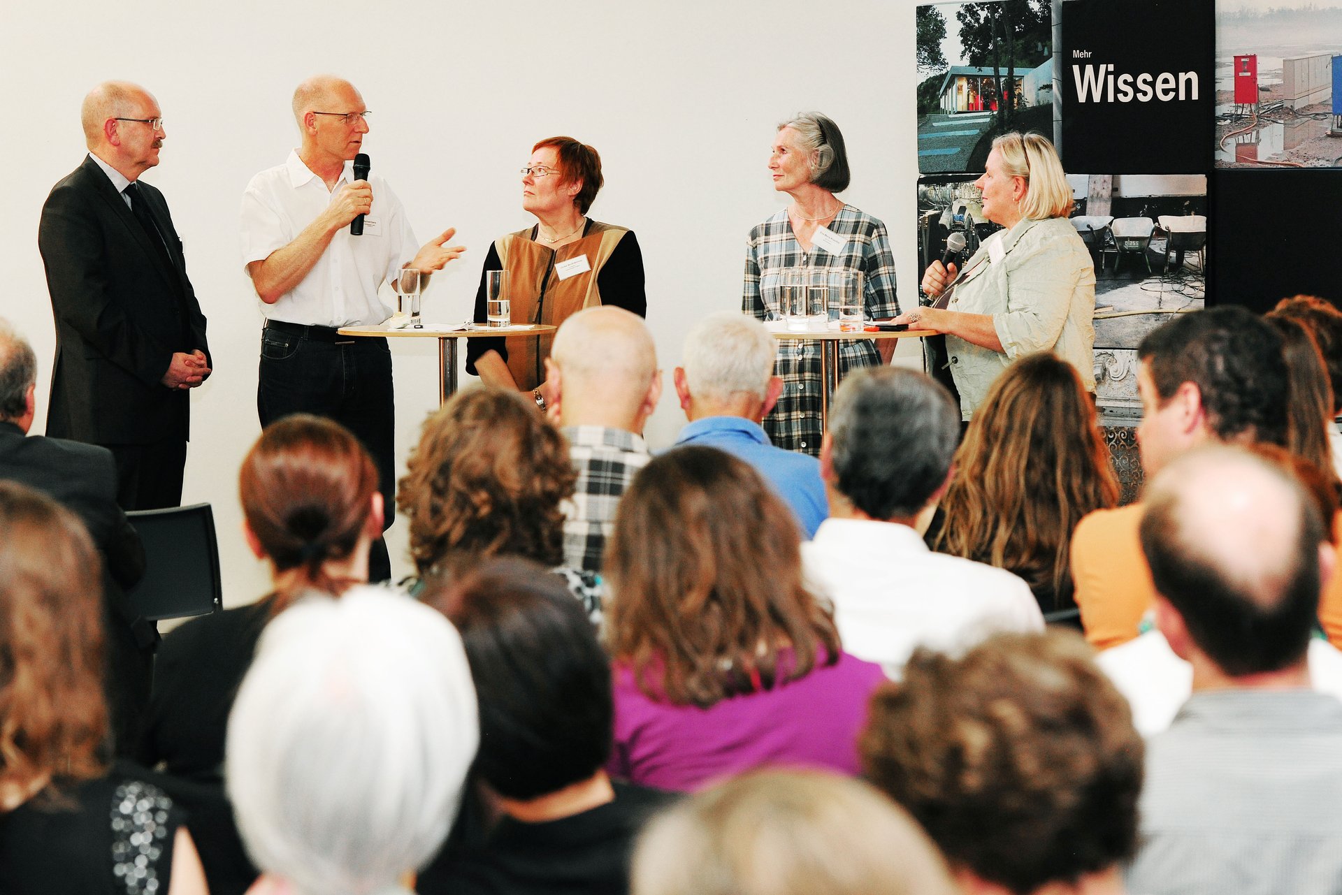 Zwei Männer und drei Frauen stehen in einer Gesprächs- und Diskussionsrunde nebeneinander. Im Vordergrund die Hinterköpfe des Publikums. (Foto: Kristina Schäfer)
