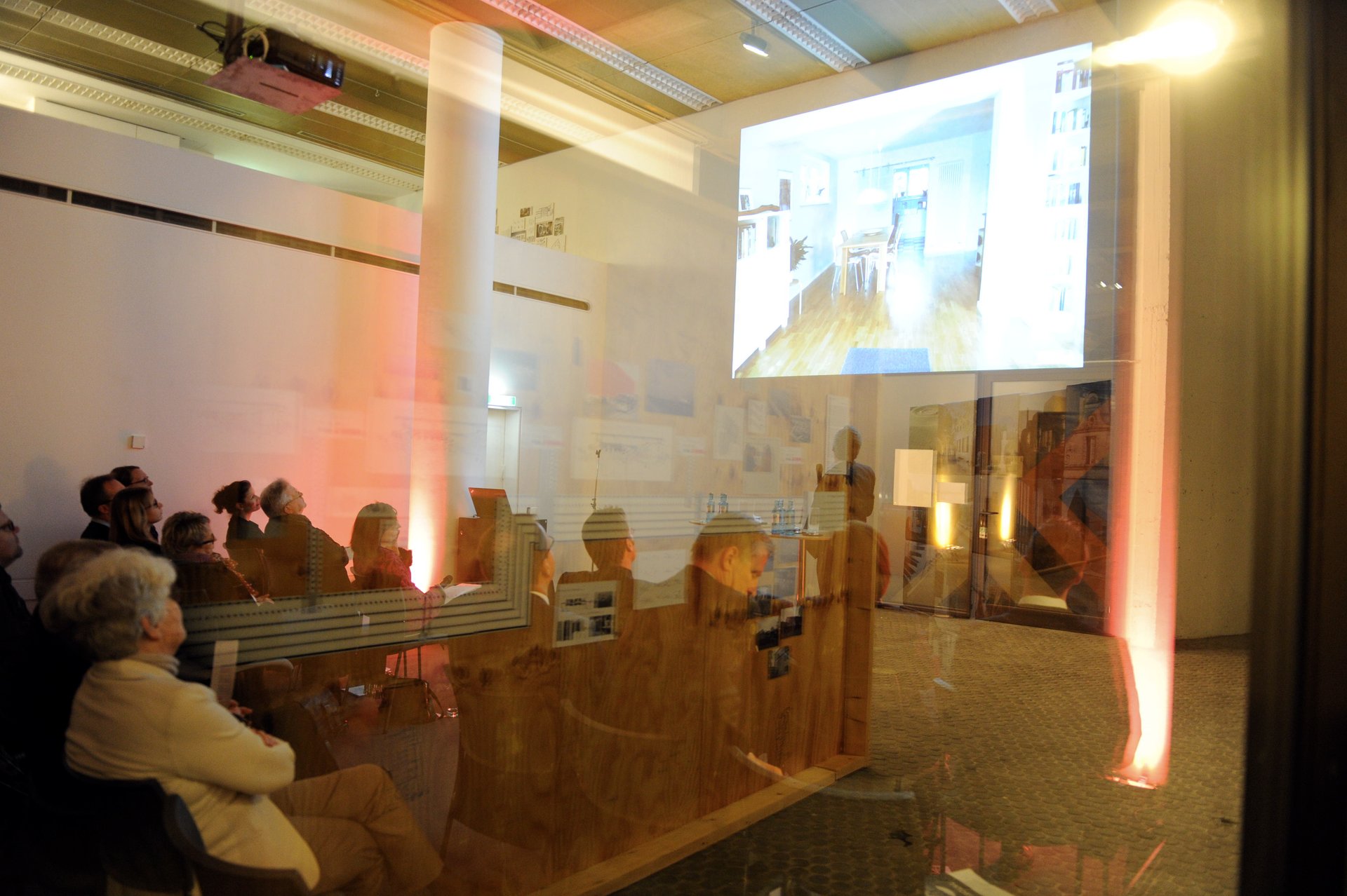 Sitzende Besucher, fotografiert durch eine Glasscheibe, die eine Präsentation hören und sehen. (Foto: Kristina Schäfer)