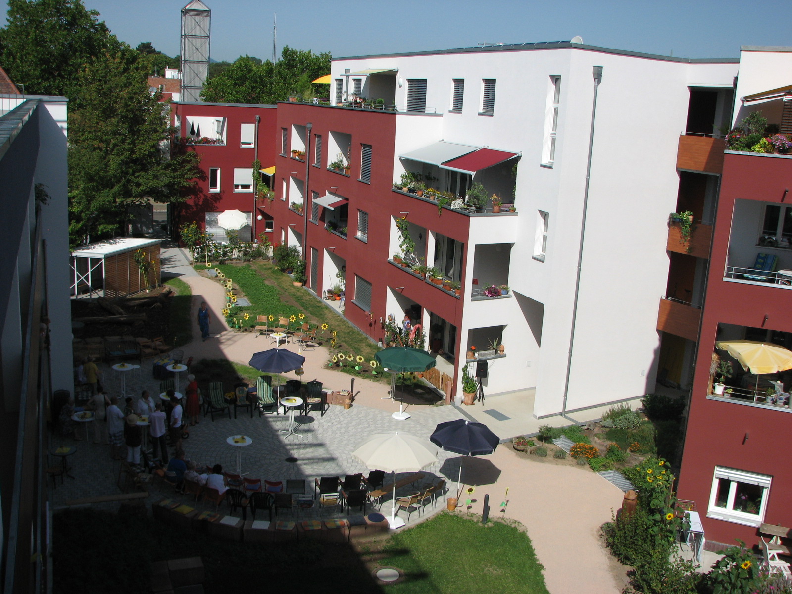 Der begrünte Innenhof eines Mehrfamilienhauses mit Balkonen und Loggien. Sonnenschirme stehen auf einer rund gepflasterten Hoffläche.  (Foto: Generationenhof Landau)